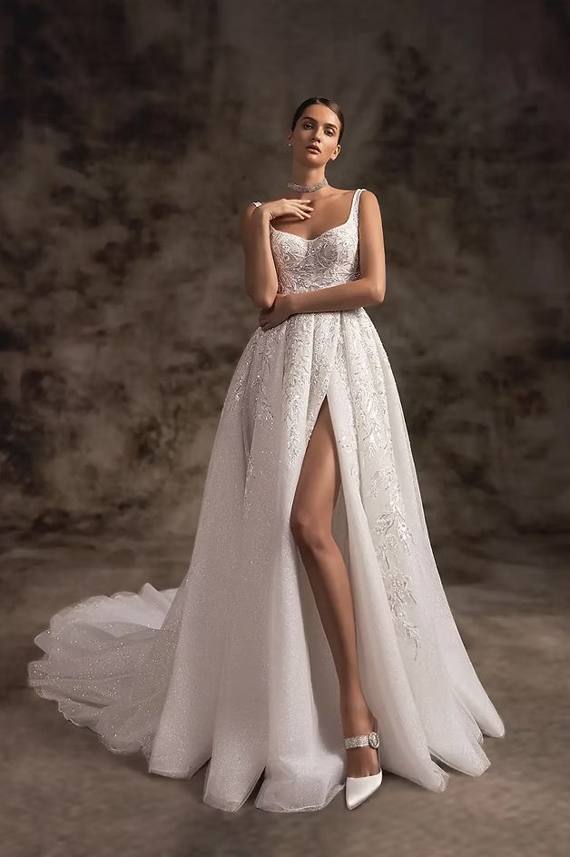 Woman in a sparkly white wedding dress with a thigh-high slit poses against a mottled background.