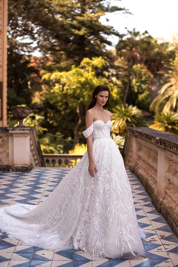 Woman in a white off-shoulder wedding dress with a long train stands on stone steps.