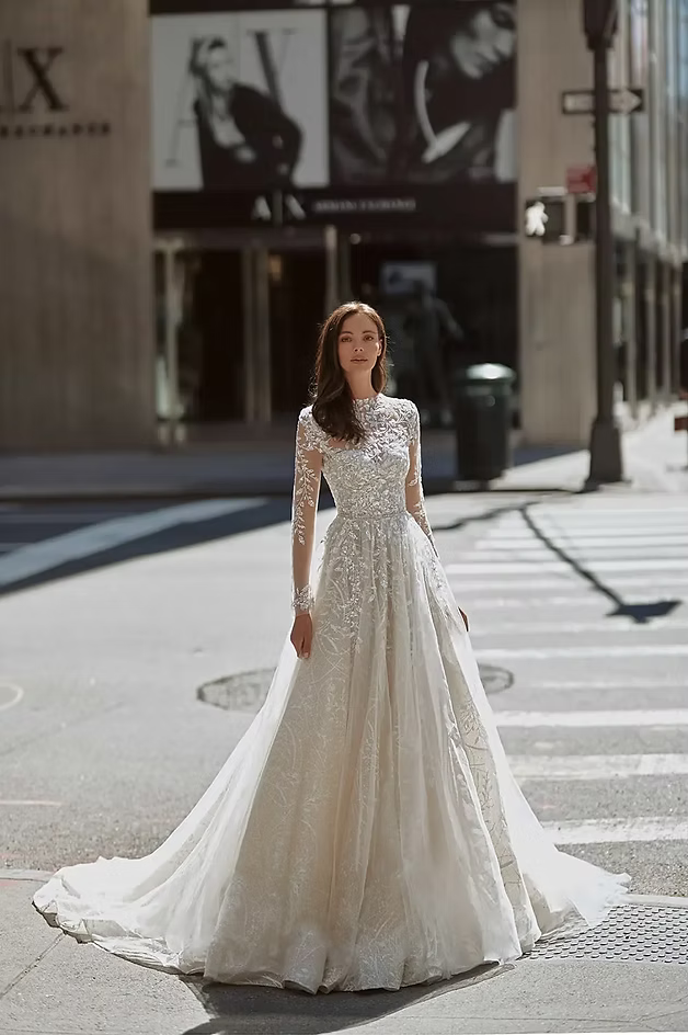 Woman in a wedding dress stands in a city crosswalk, facing the camera; sunlight.