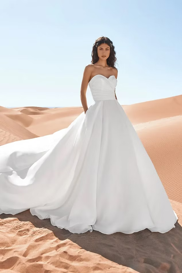 Woman in white strapless wedding dress with train poses in desert landscape.