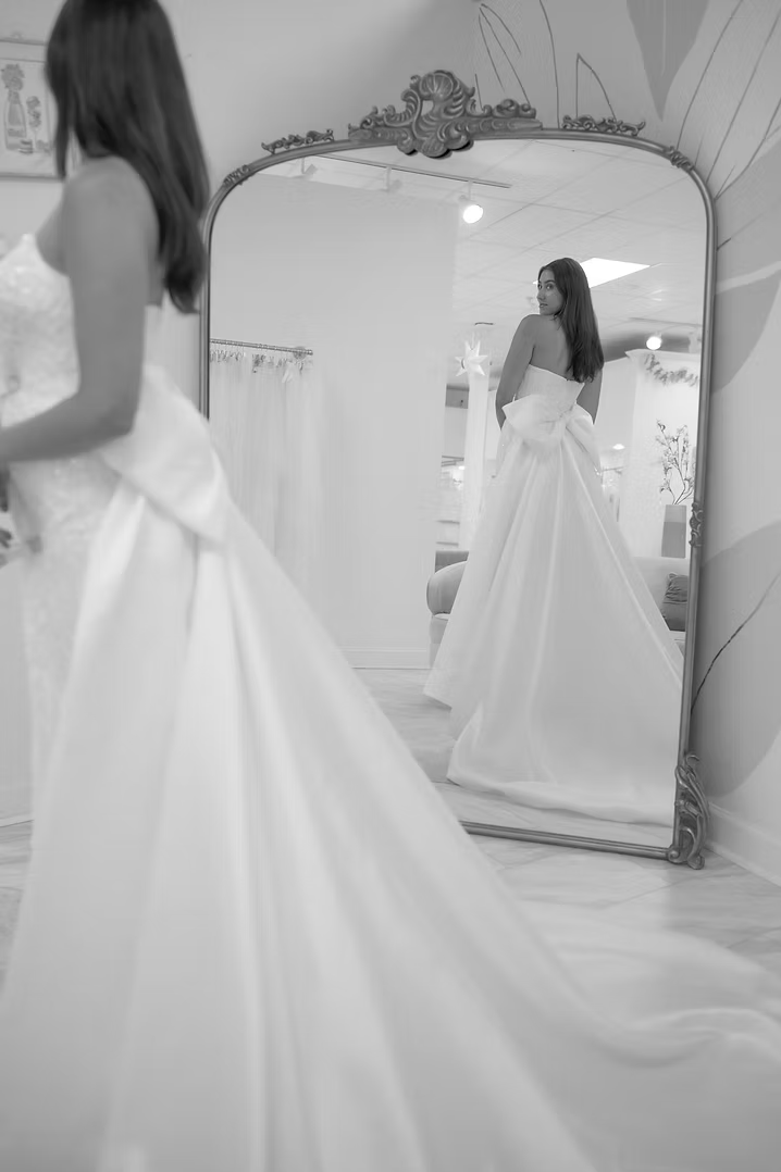 Bride in wedding dress, looking in ornate mirror.