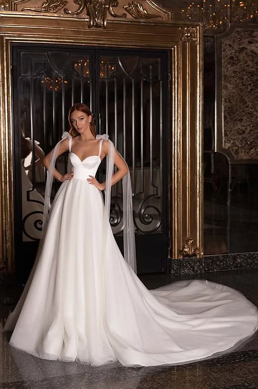 Woman in white wedding dress with long train, standing in a fancy doorway.