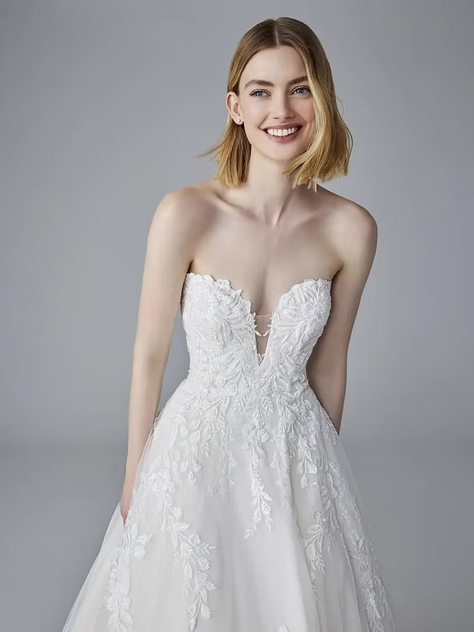 Woman in a strapless white wedding dress with lace detailing, smiling.