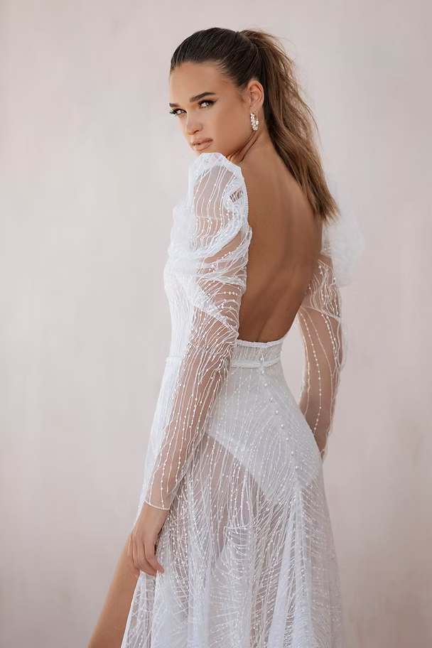 Woman in white sequined dress with open back, looking over shoulder.
