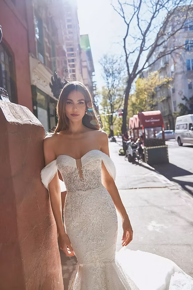 Woman in a sparkly, off-the-shoulder wedding dress stands outdoors.