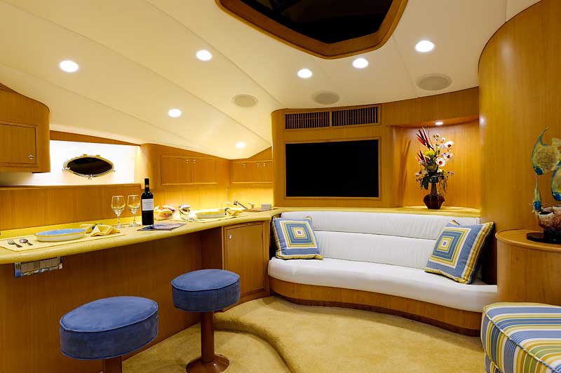 A living room on a boat with a couch , bar , and television.
