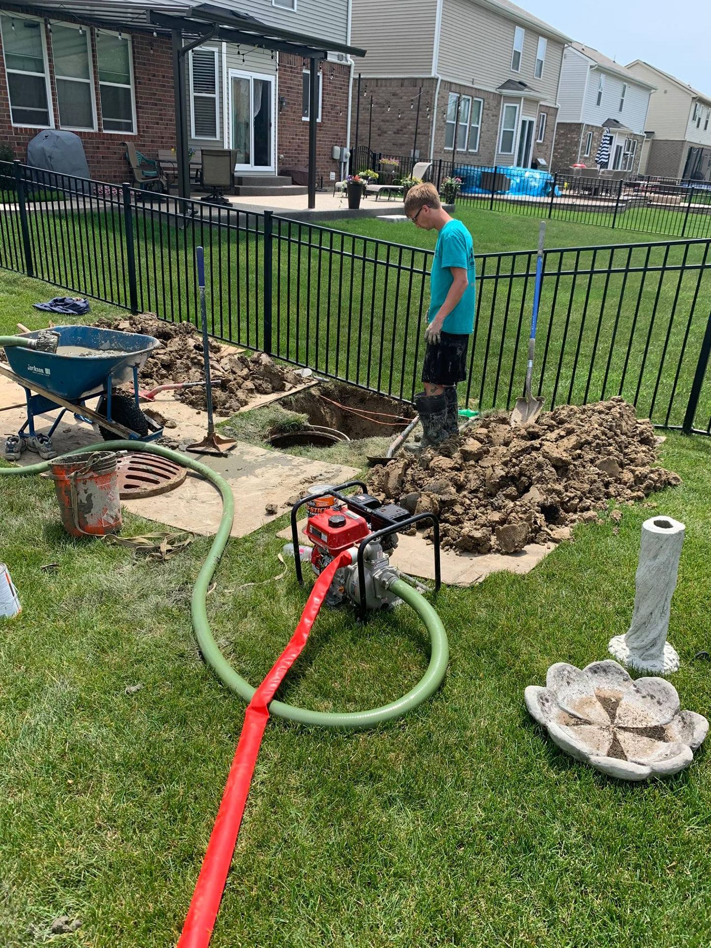 Boy looking at excavation in backyard with pump and hose.