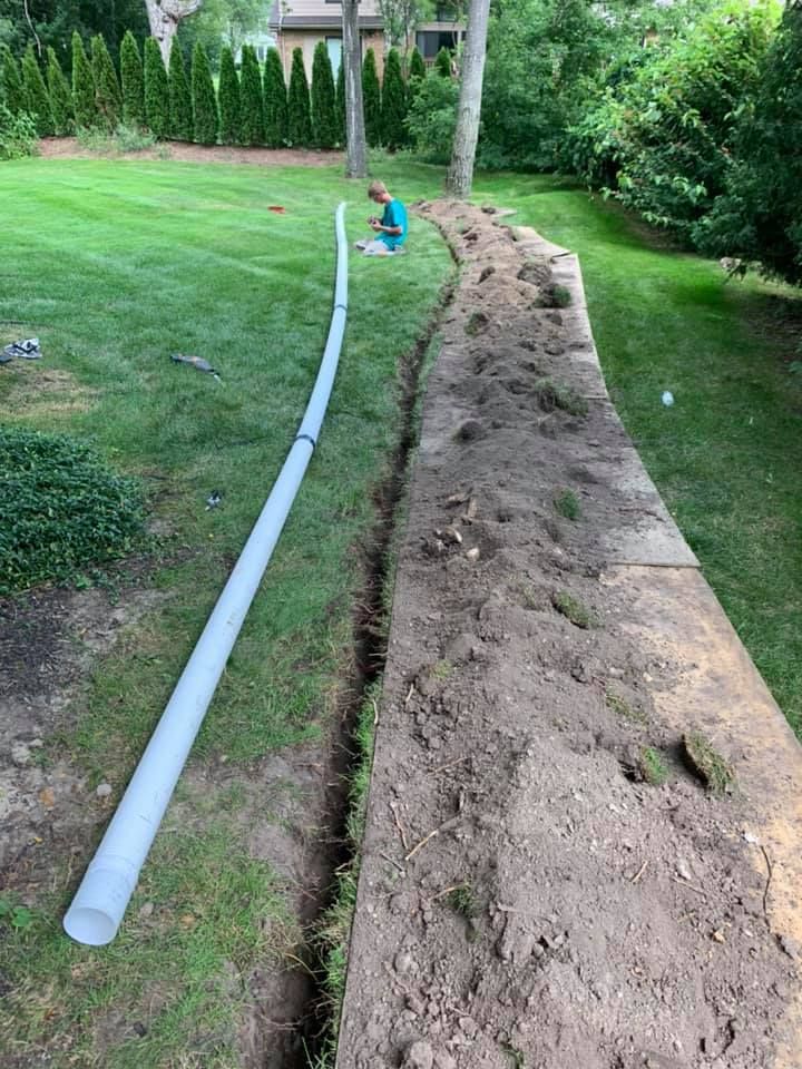 A person working on a trench in a grassy yard, with a pipe lying nearby.