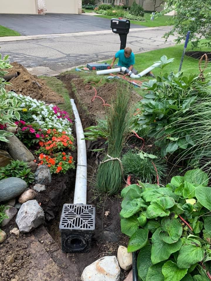 Man installing drainage system in garden, pipe extends from black grate to upper ground.