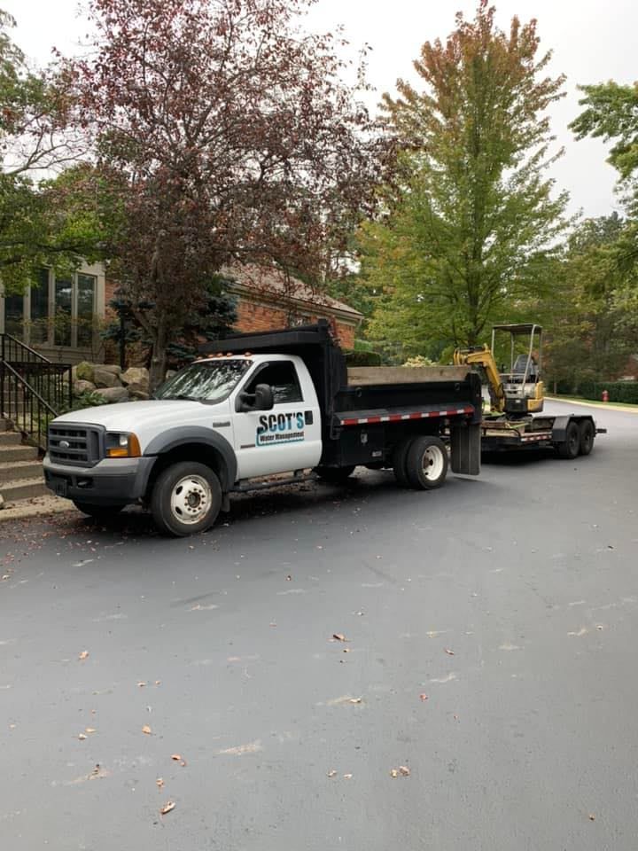 White dump truck with excavator on trailer parked on asphalt driveway.