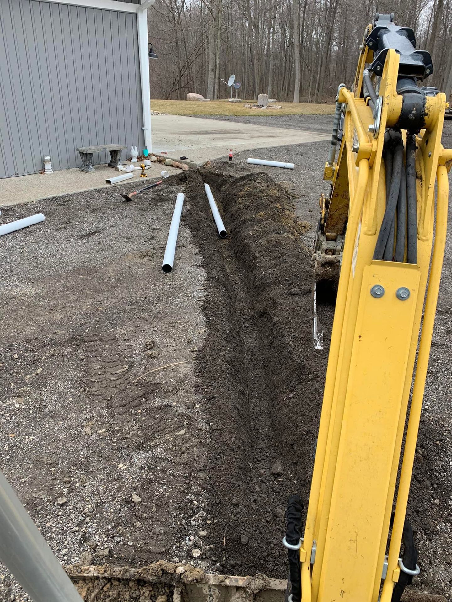 Yellow excavator digging a trench, white pipes laid along the ground.