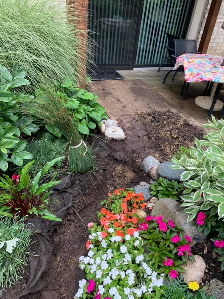 Garden bed with colorful flowers, rocks, and a newly planted bundle of grass near a patio door.