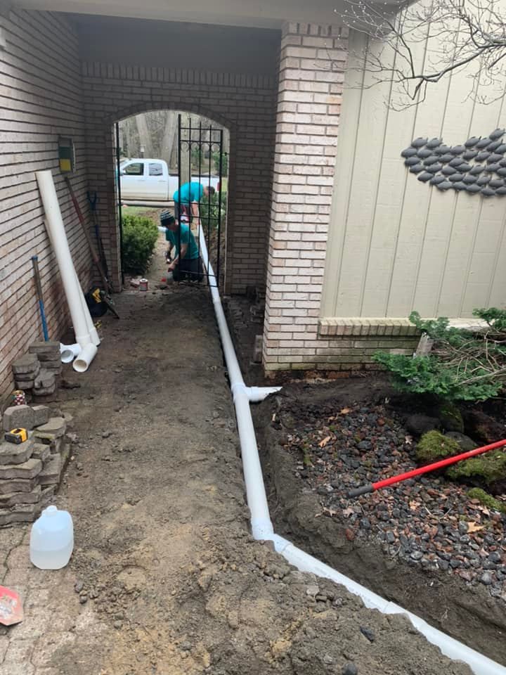 Workers installing white drainage pipe along a building's walkway.