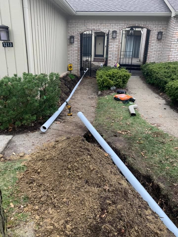 Trench dug with PVC pipes installed, leading to a house. Construction in progress.