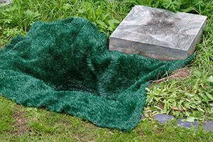 A green blanket is covering a grave in the grass.
