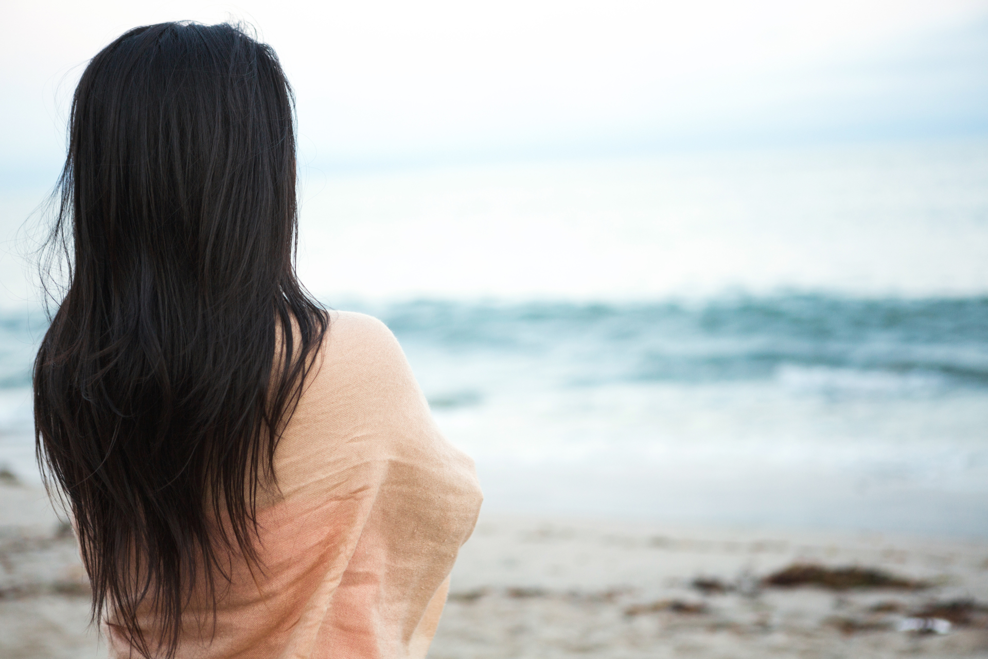 A woman is standing on a beach looking at the ocean.