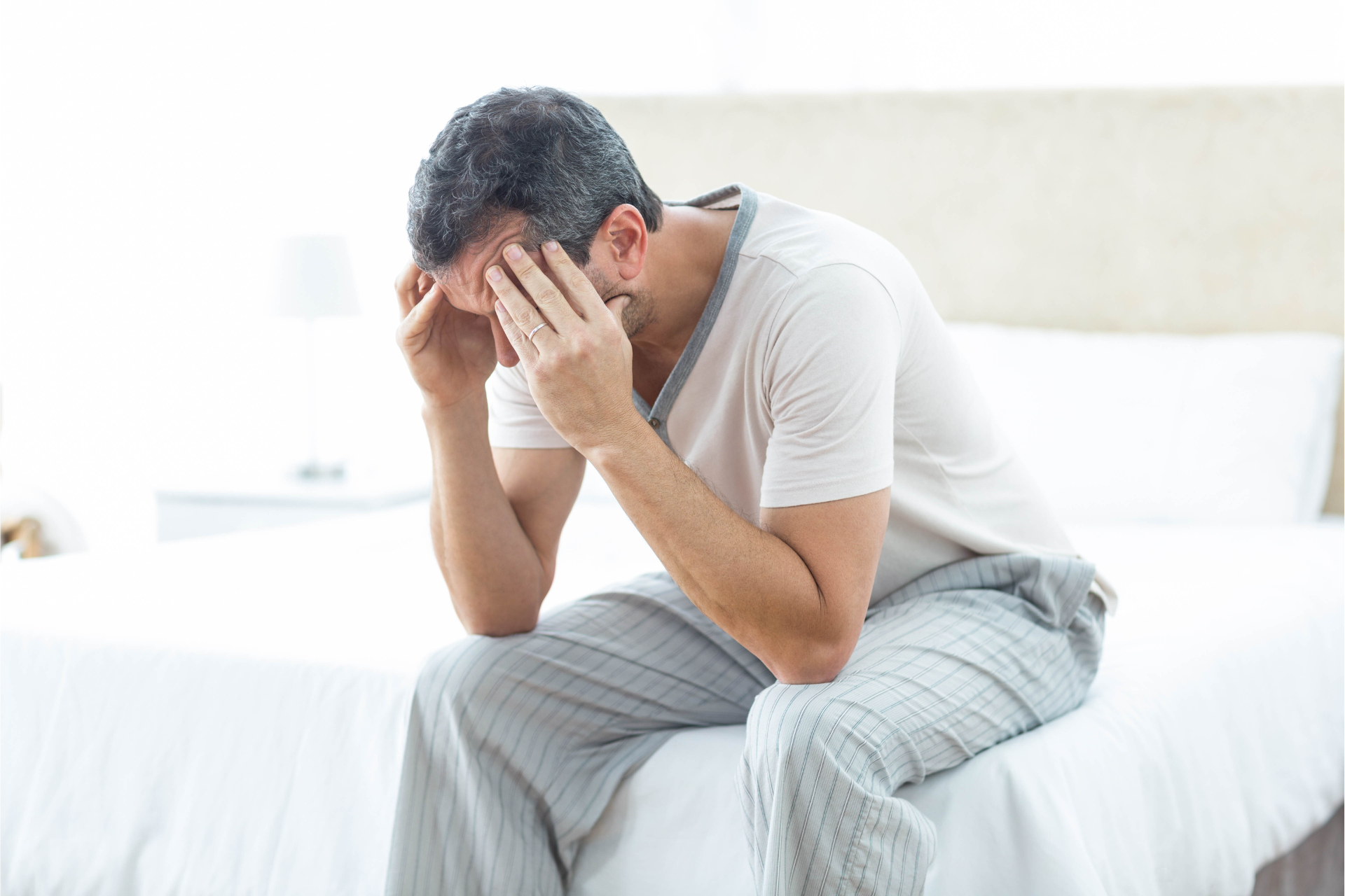 A man is sitting on a bed with his head in his hands.