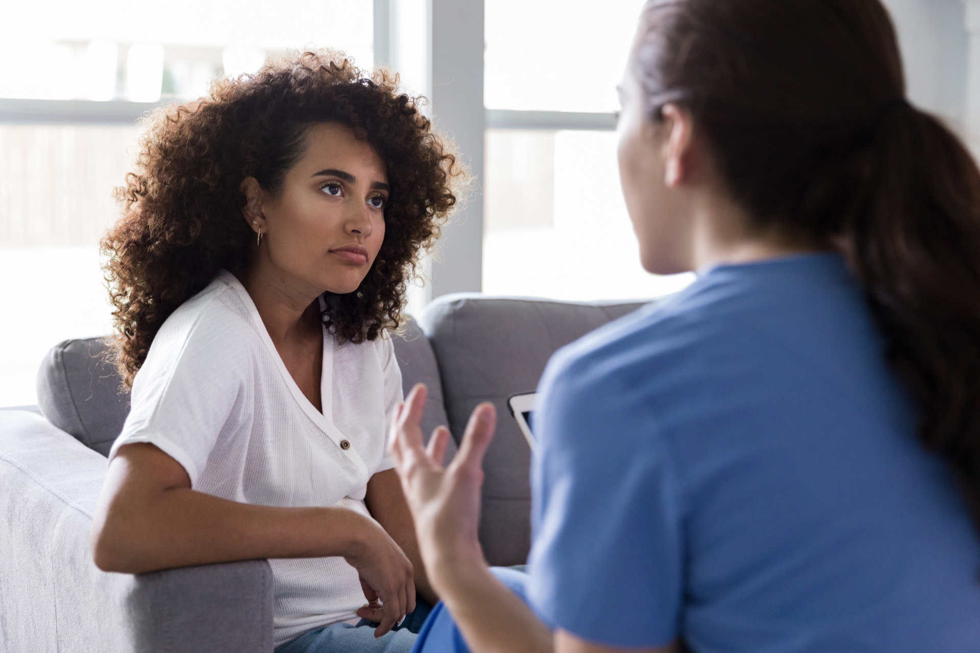 A woman is sitting on a couch talking to another woman.