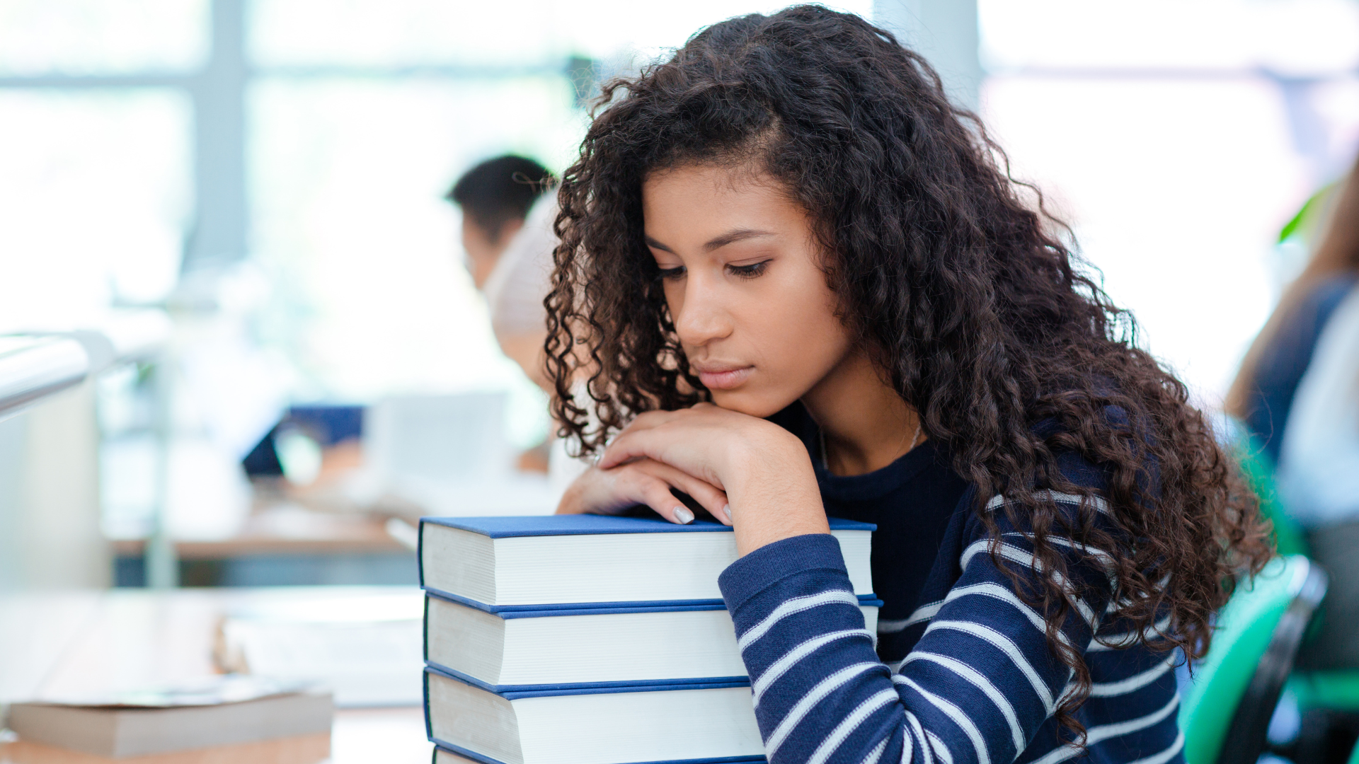 A young woman is sitting at a table with a stack of books.