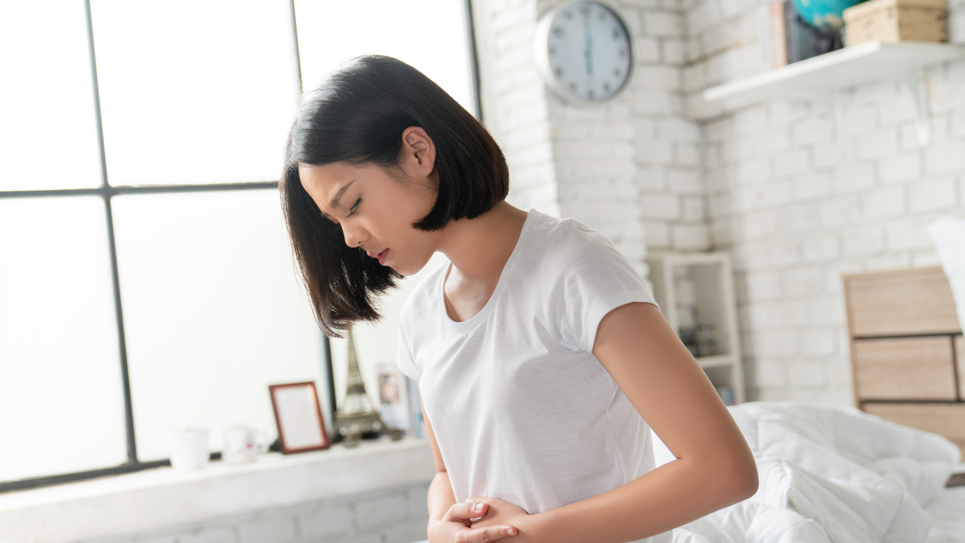 A woman is sitting on a bed holding her stomach.