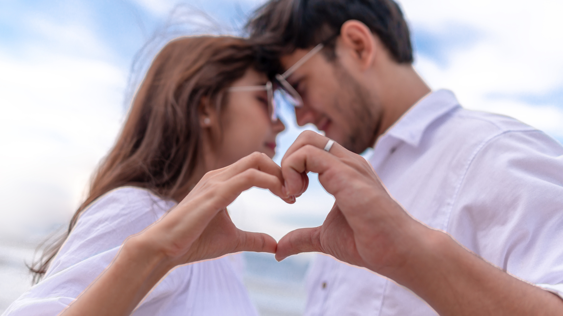 A man and a woman are making a heart shape with their hands.