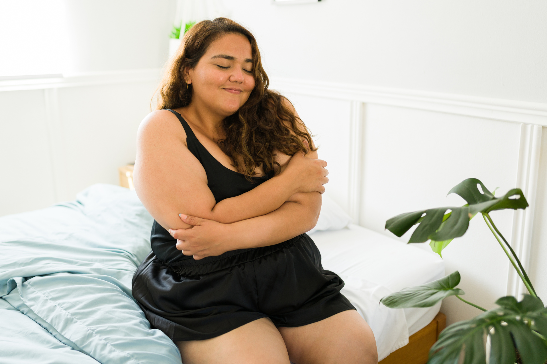 A woman is sitting on a bed hugging herself.