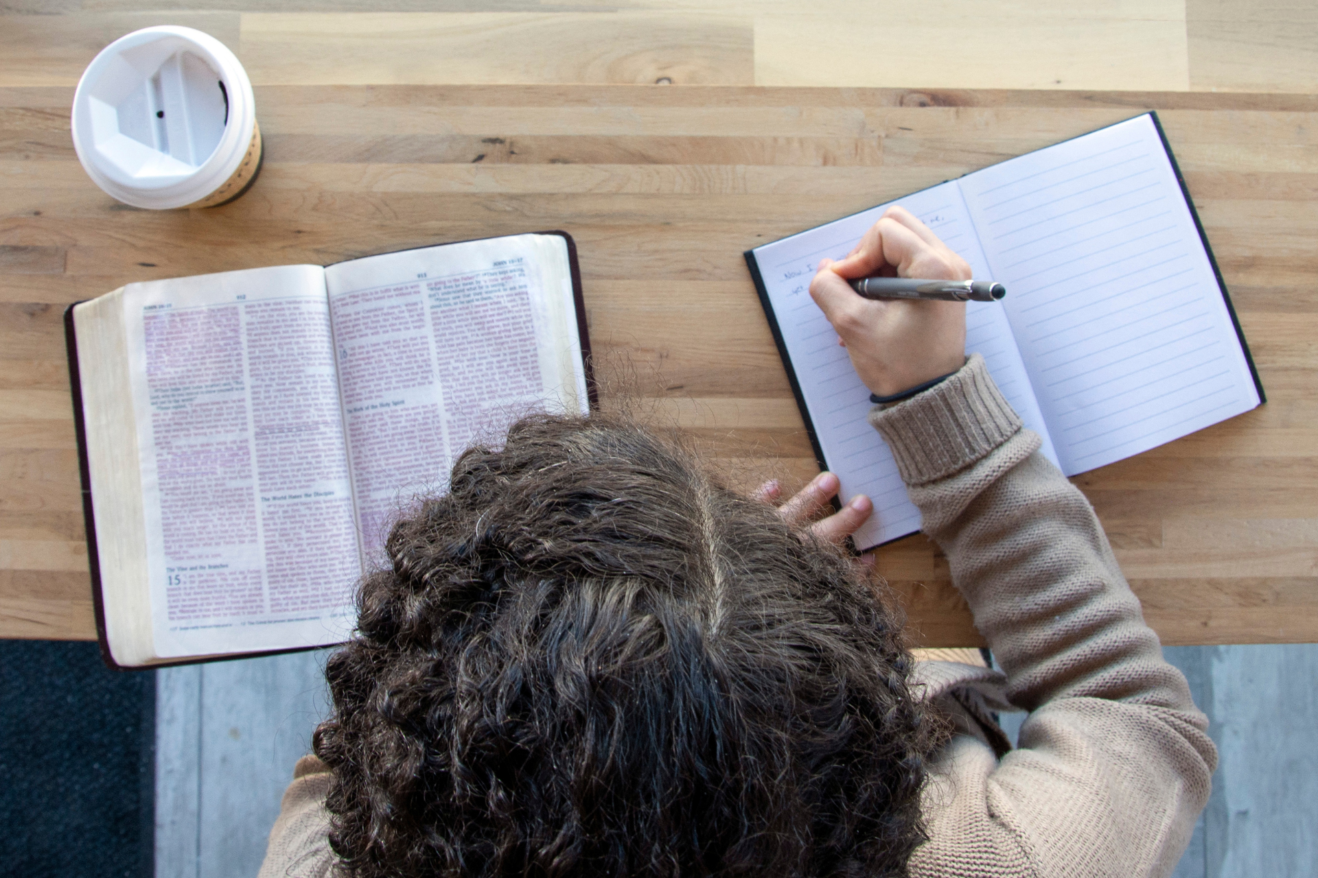 A woman is sitting at a table writing in a notebook.