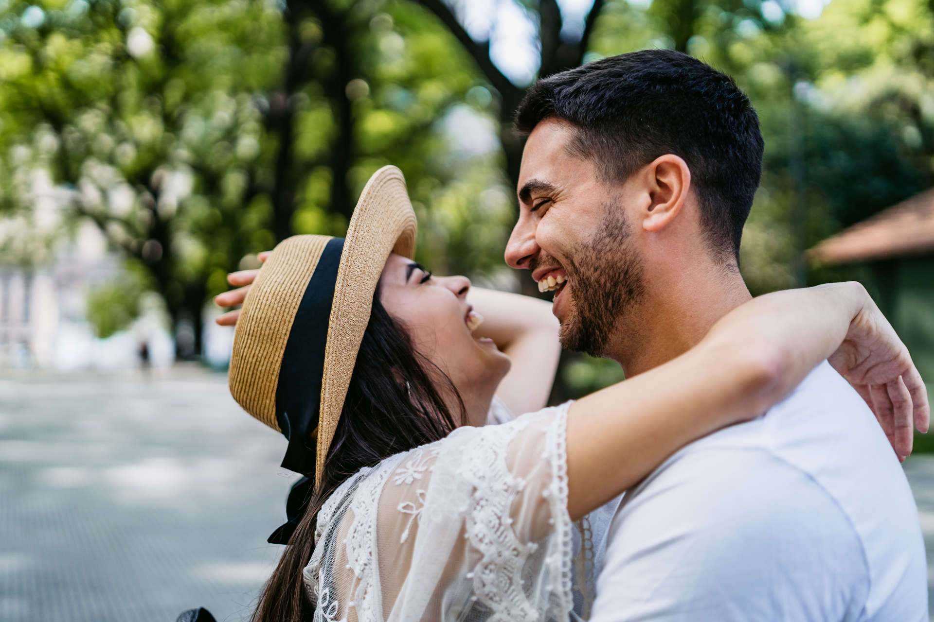 A man and a woman are hugging each other in a park . the woman is wearing a straw hat.