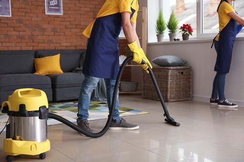 A man and a woman are cleaning a living room with a vacuum cleaner.