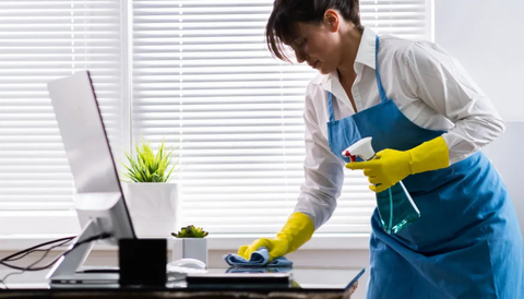 A woman in a blue apron and yellow gloves is cleaning a desk.