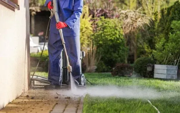 A man is using a high pressure washer to clean a sidewalk.