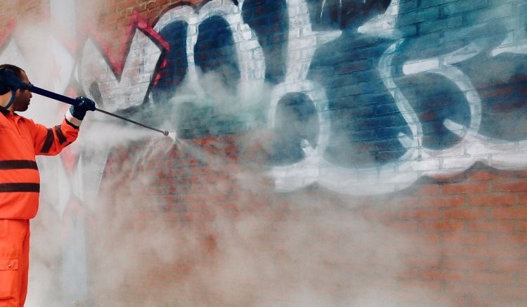 A man is cleaning graffiti on a brick wall with a high pressure washer.