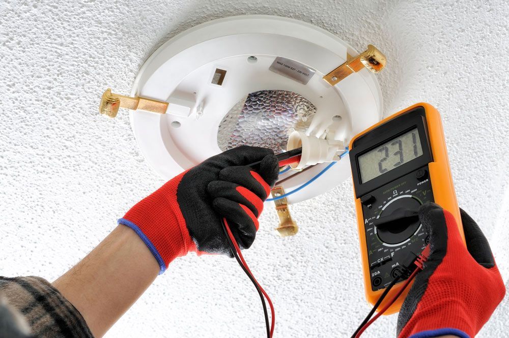 A Man is Using a Multimeter to Test a Light Fixture — Himec Electrical In Withcott, QLD