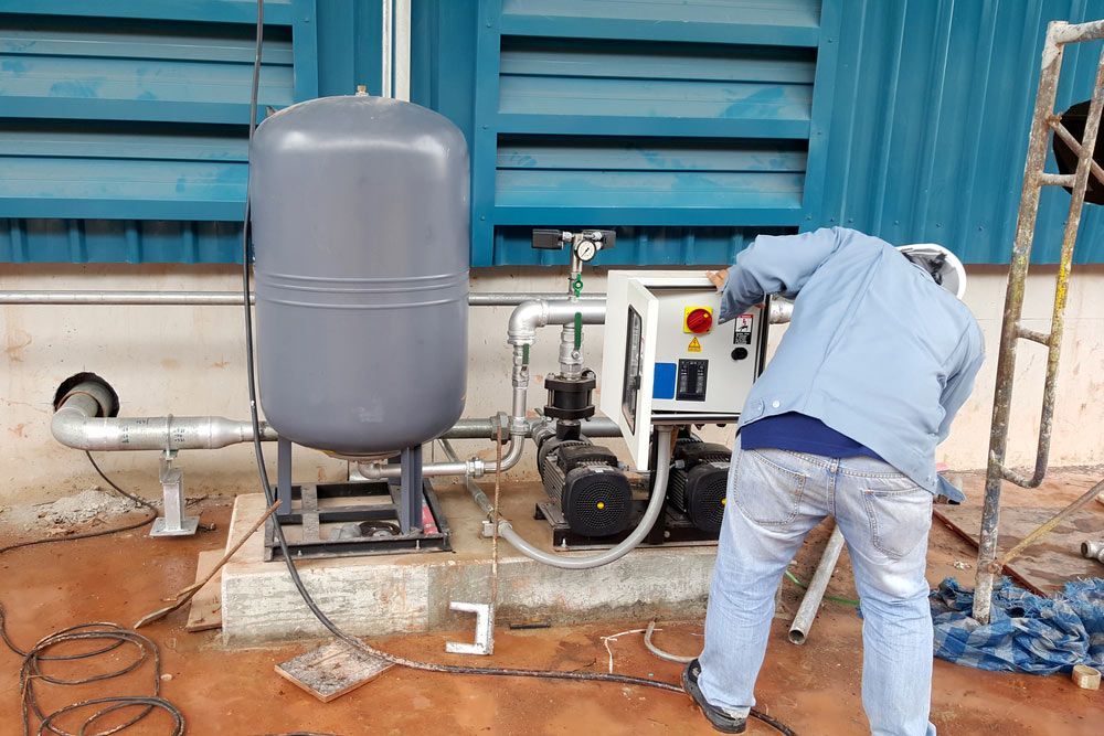 A Man is Working on a Water Pump Outside of a Building — Himec Electrical In Withcott, QLD