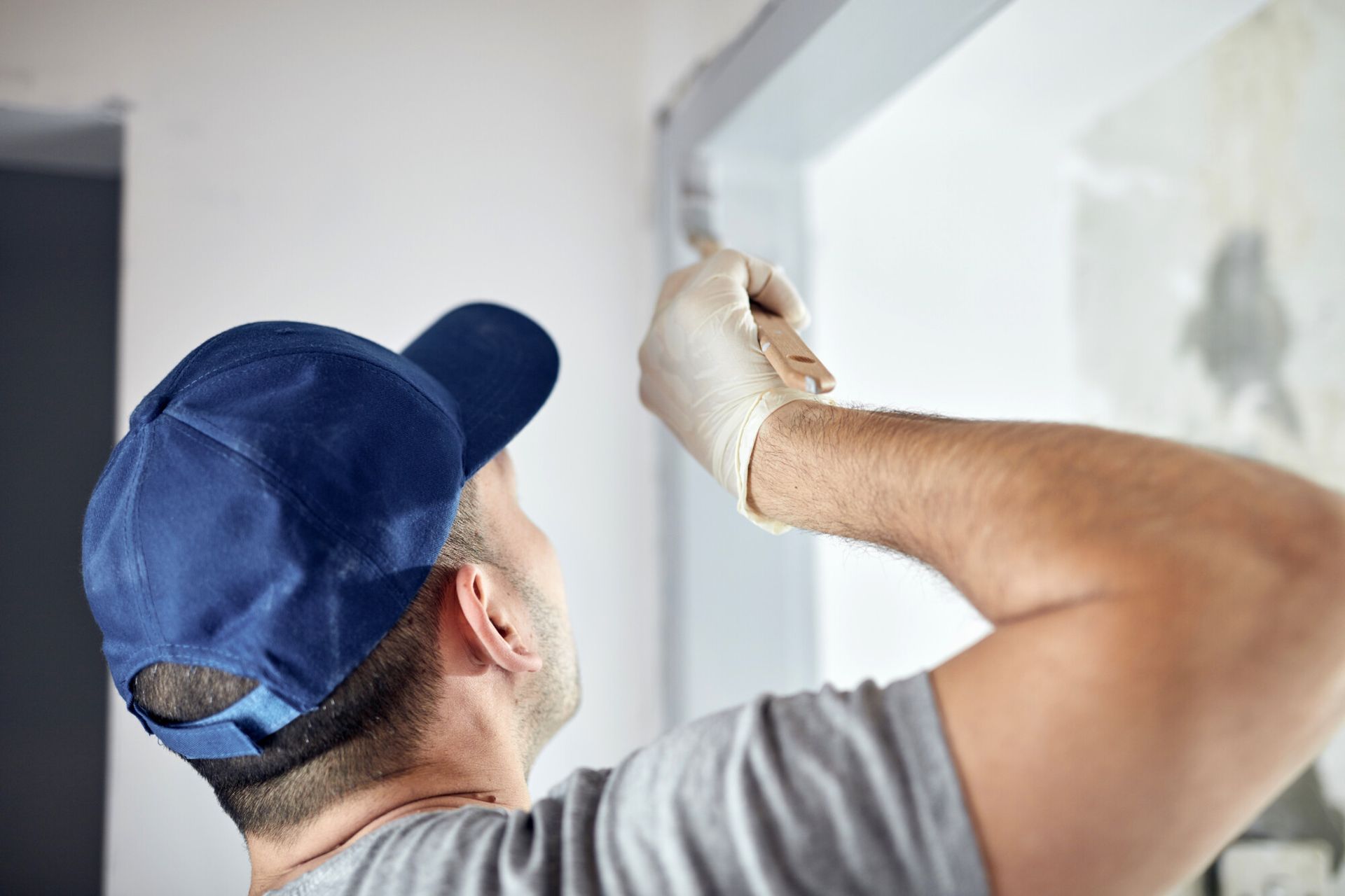 Man Wearing a Blue Hat and Gloves is Painting a Wall – Naples, FL – A Choice Painting