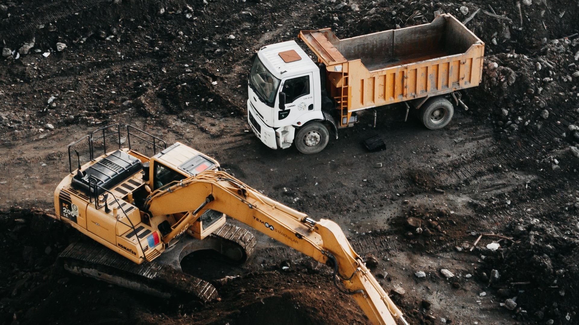 A yellow excavator is loading dirt into a dump truck.