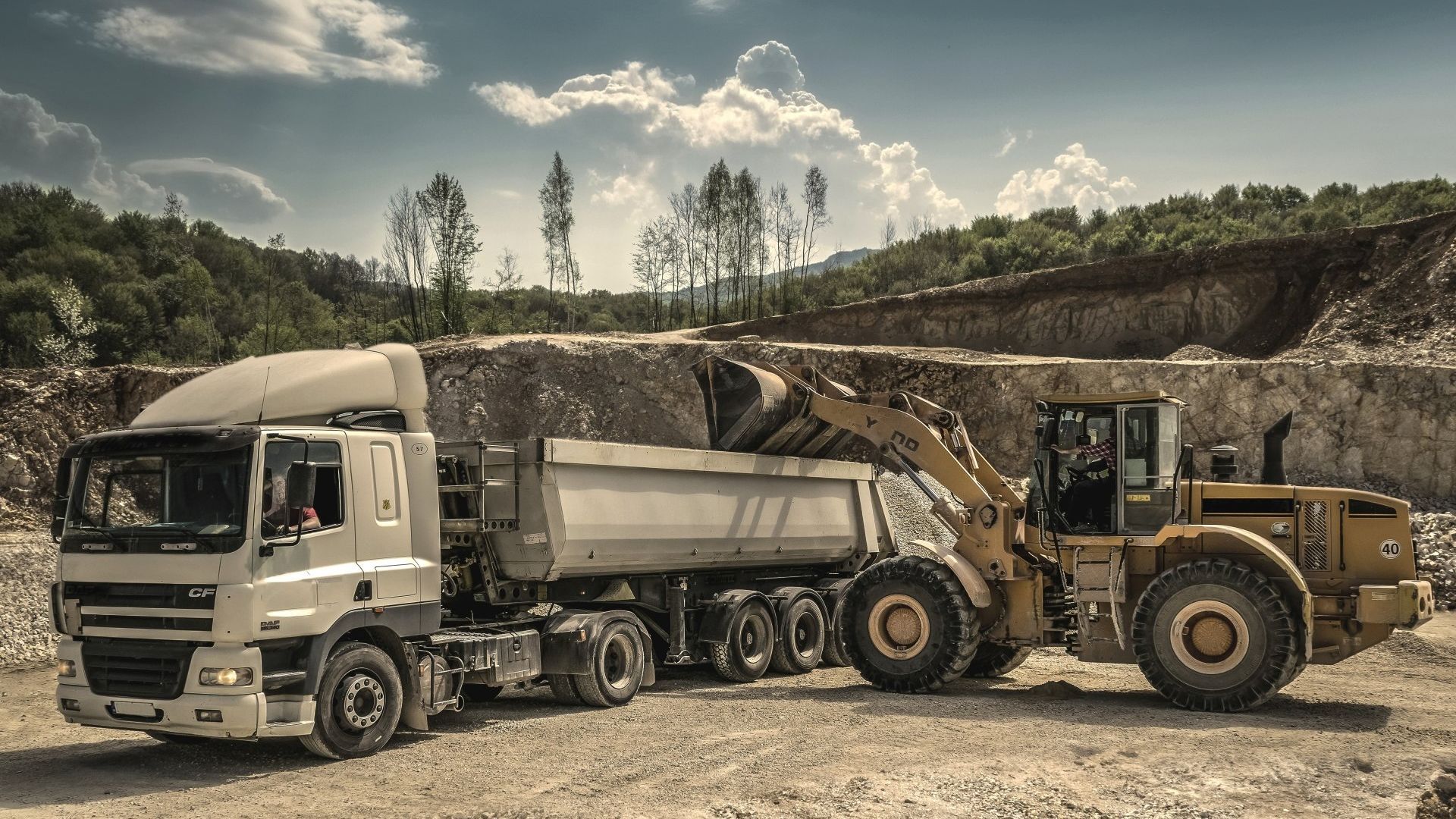 A dump truck is being towed by a bulldozer in a quarry.