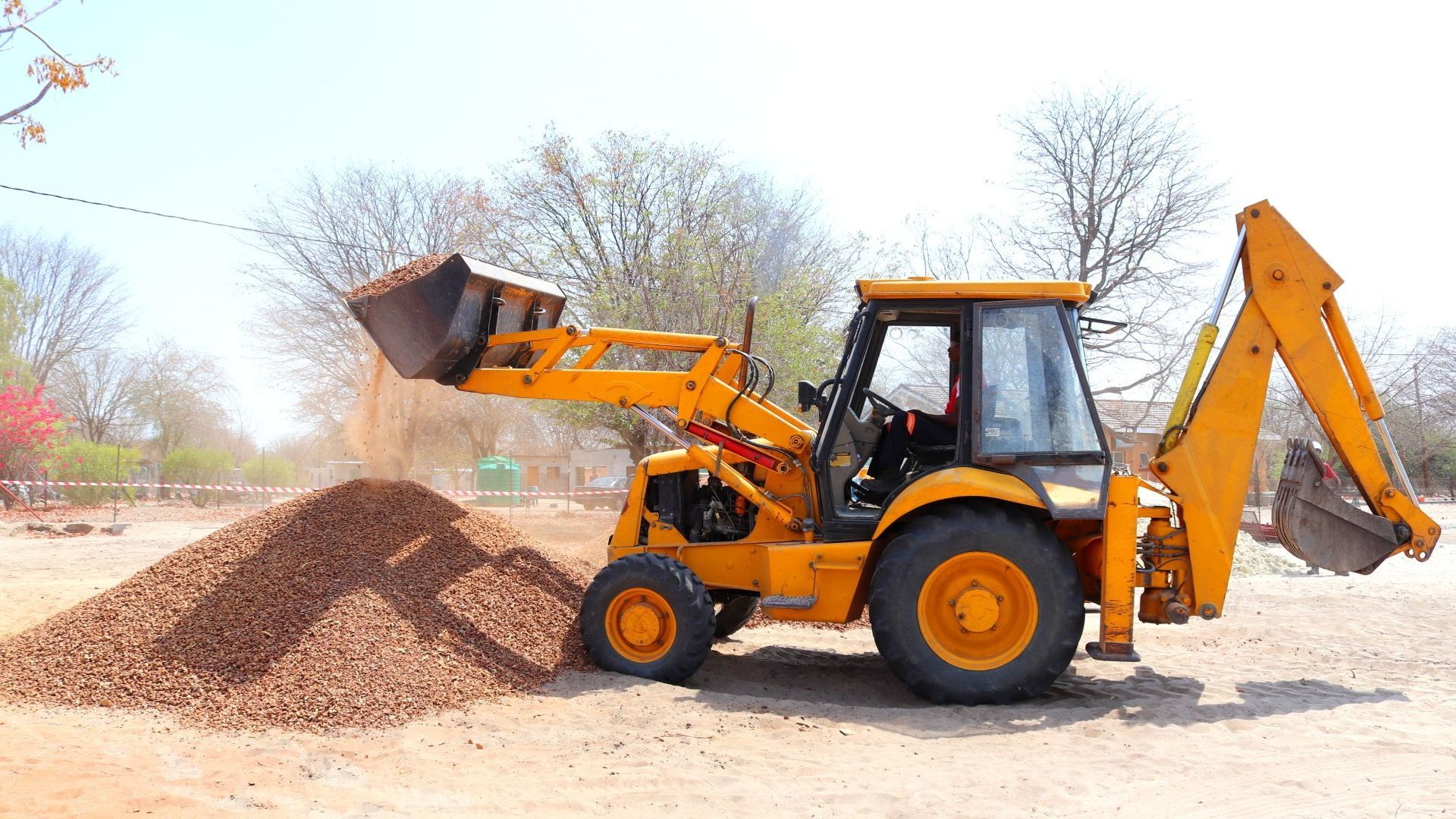 A yellow excavator is loading dirt into a pile.