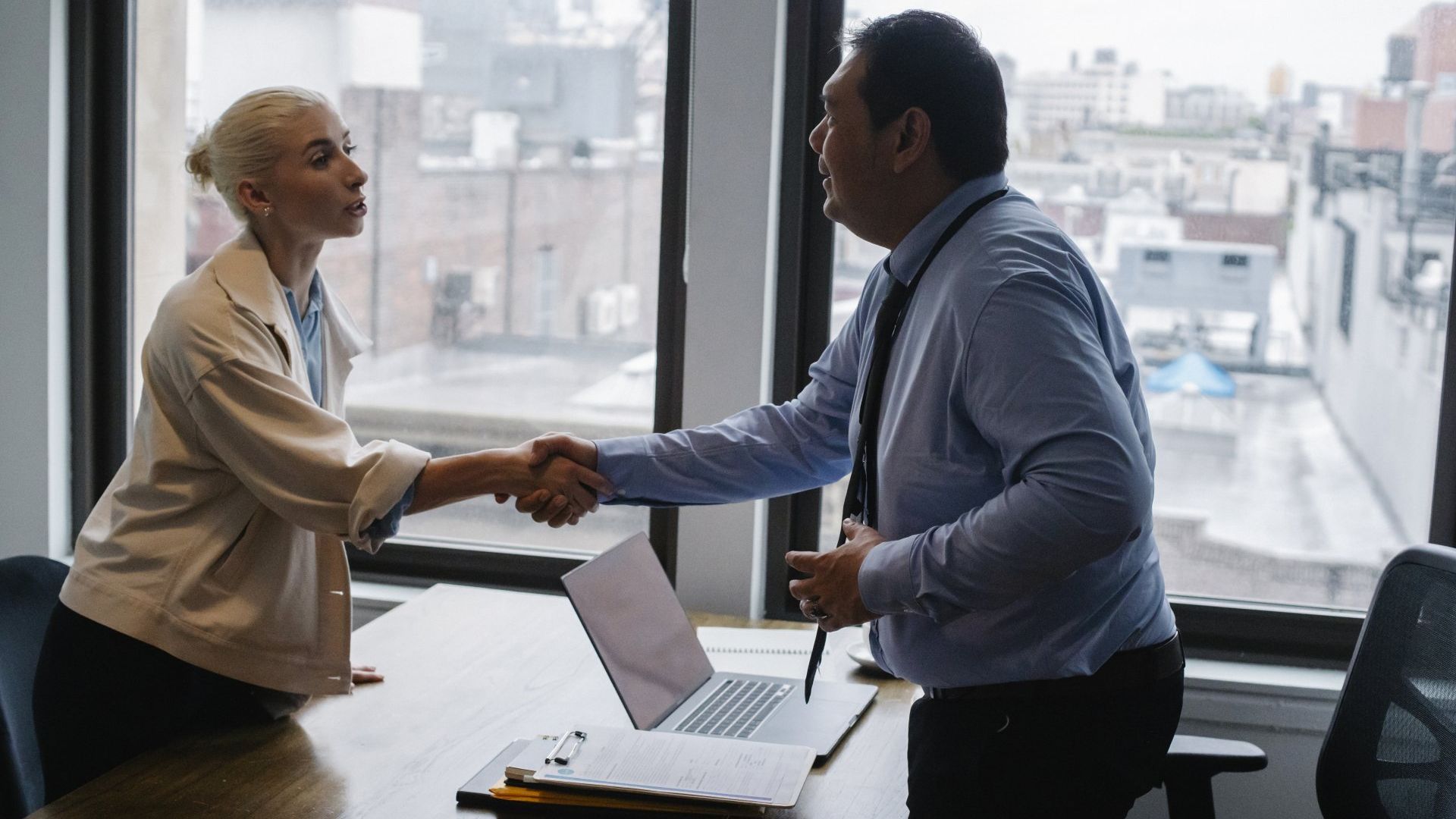 A man and a woman are shaking hands in an office.