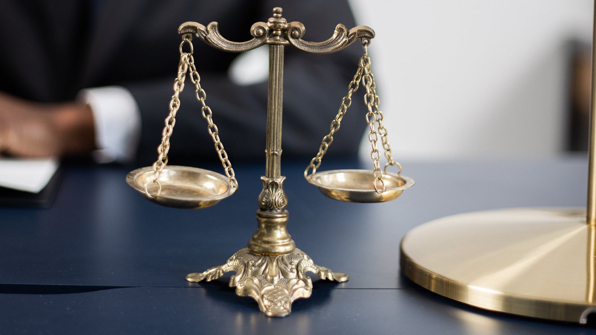 A scale of justice is sitting on a table with a man in the background.