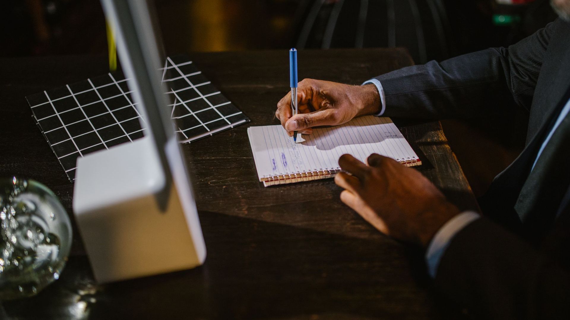 A man in a suit is sitting at a table writing in a notebook.