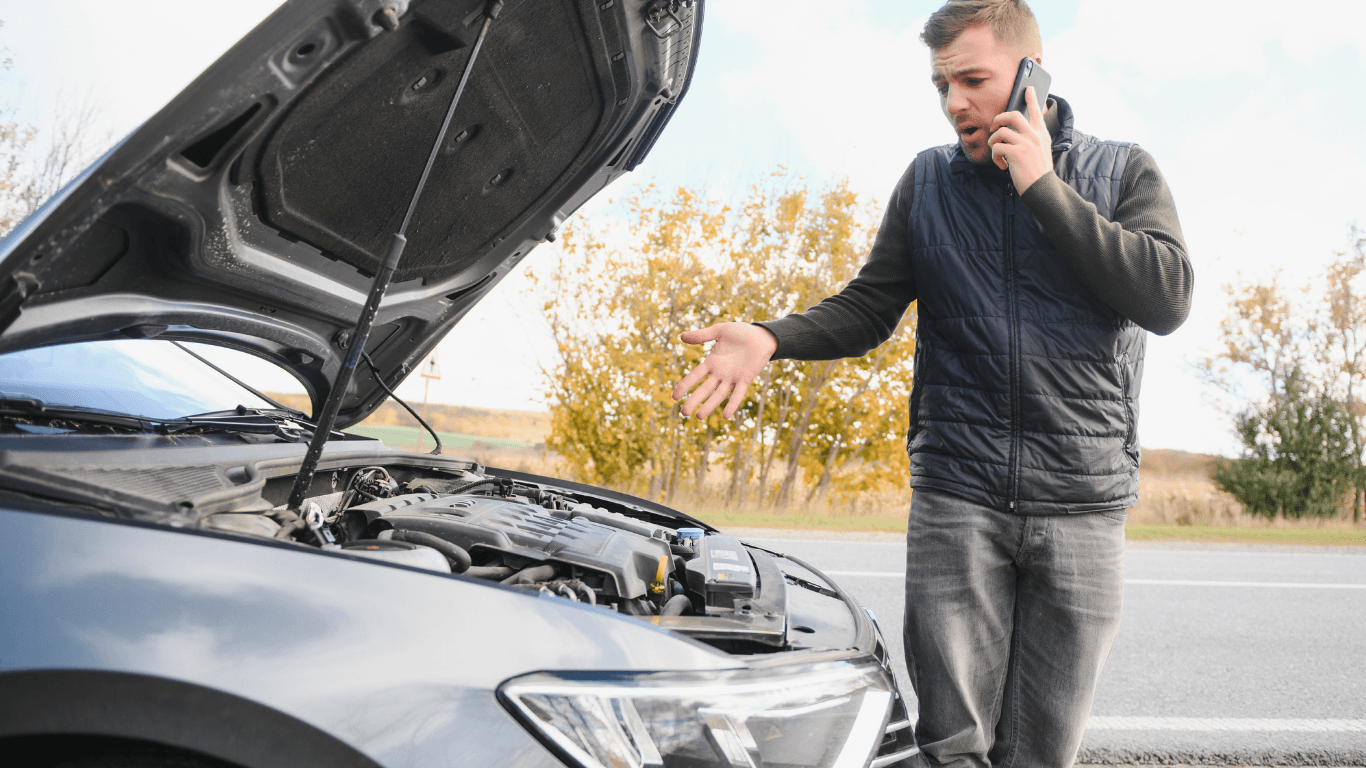 A person calling a mechanic for help outside a broken down vehicle