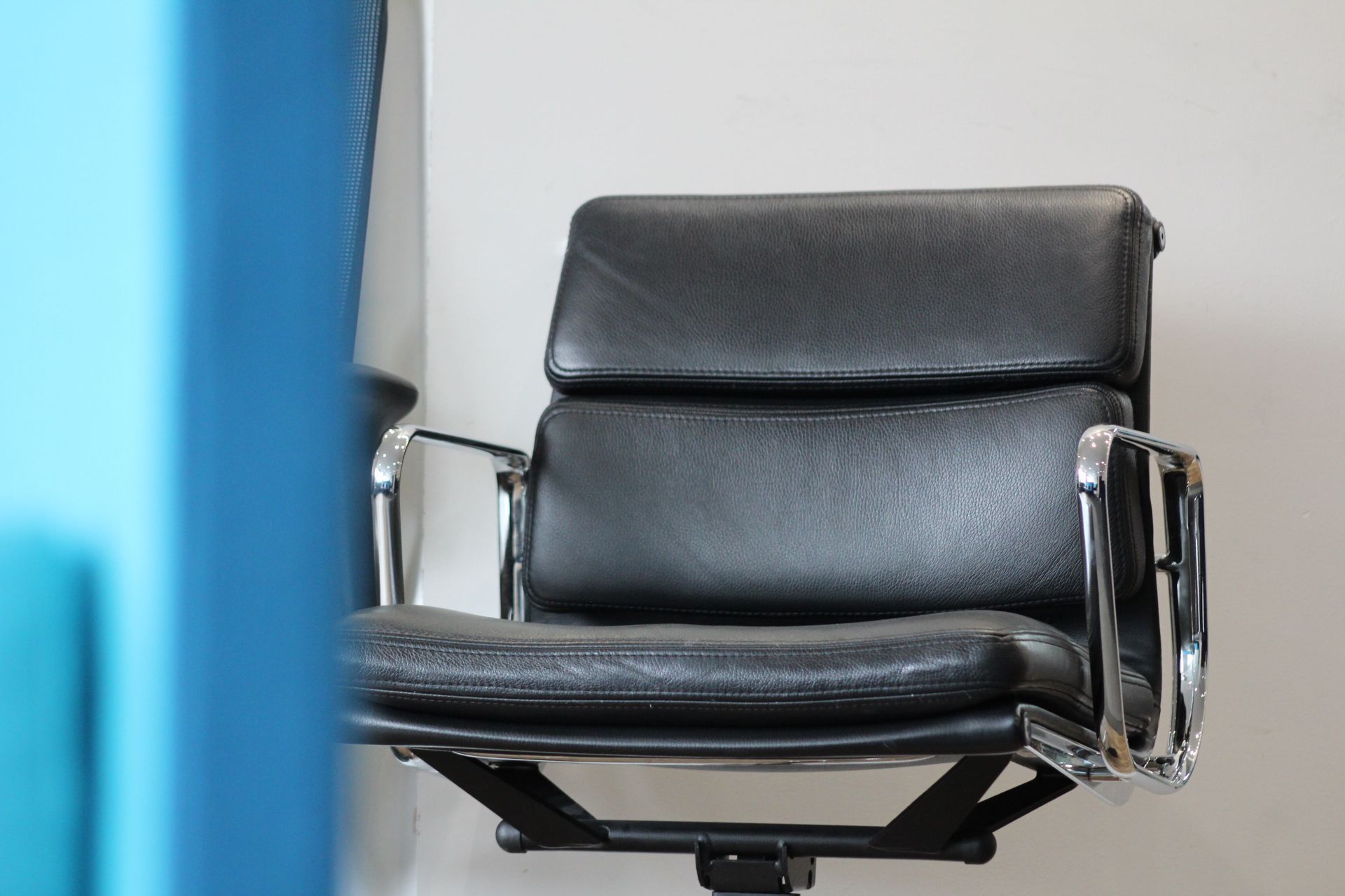 Black leather office chair against a white wall; blue edge in the foreground.