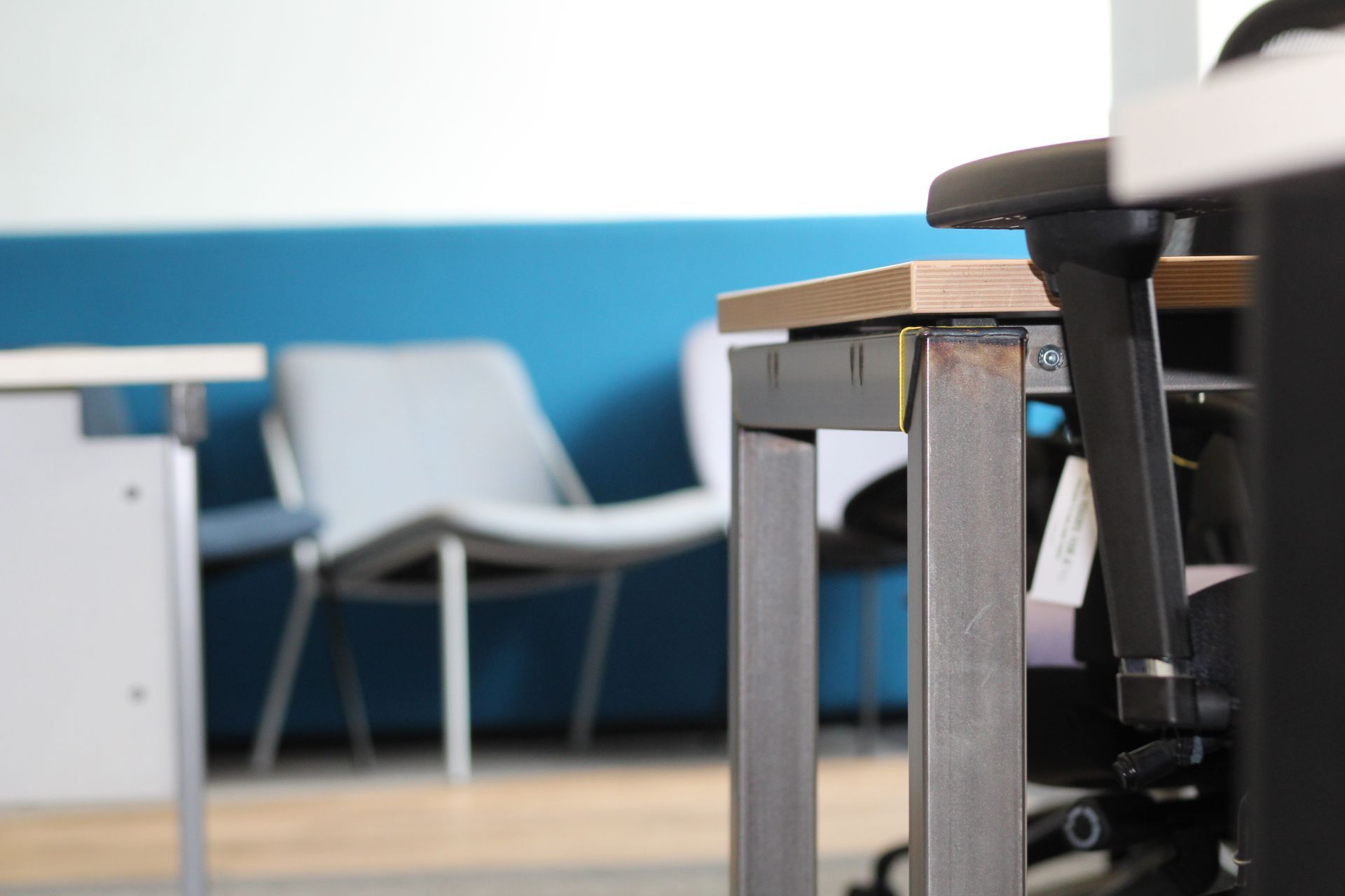 Close-up of a desk with metal legs in an office setting. A chair and wall with blue paint are in the background.