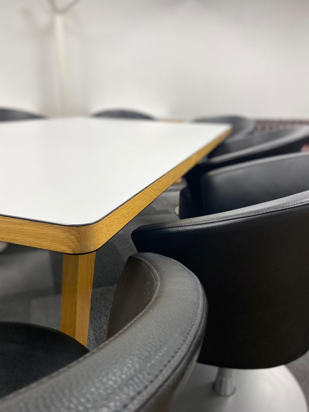 White tabletop with wooden edge, surrounded by black chairs.