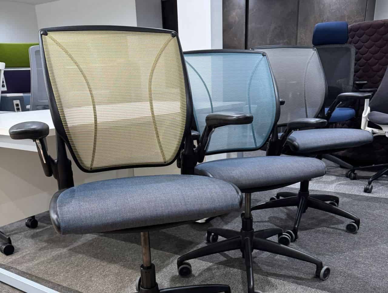 Several office chairs in a row. The chairs have mesh backs in various colors and gray seats.