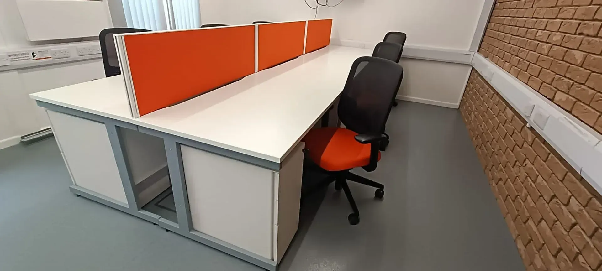 An office desk with orange dividers and chairs in front of a brick wall.