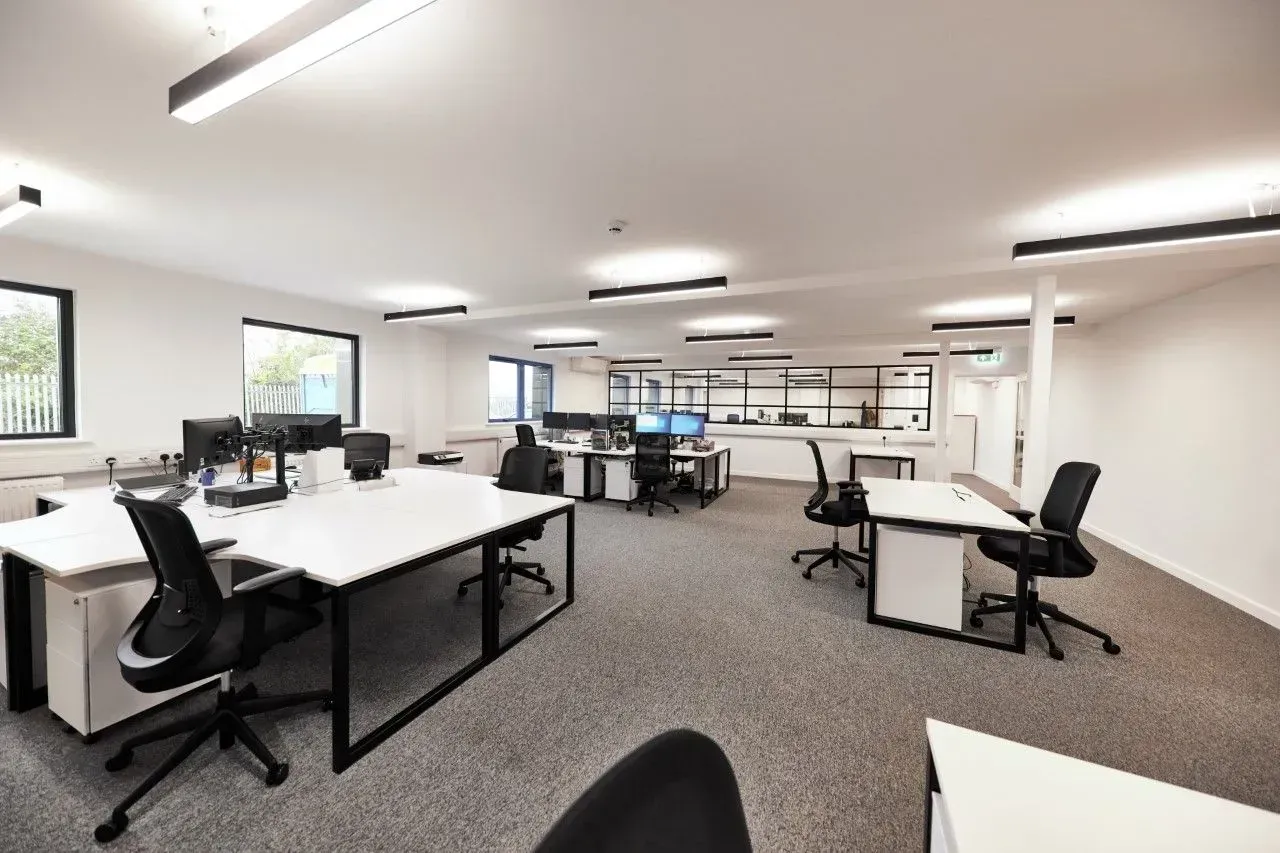Bright office space with white desks, black chairs, and computers. Gray carpet.