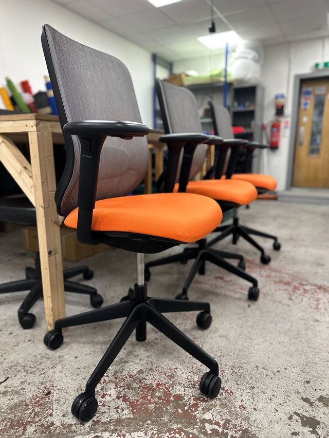 Refurbished task chairs with new orange seat fabric lined up in the workshop