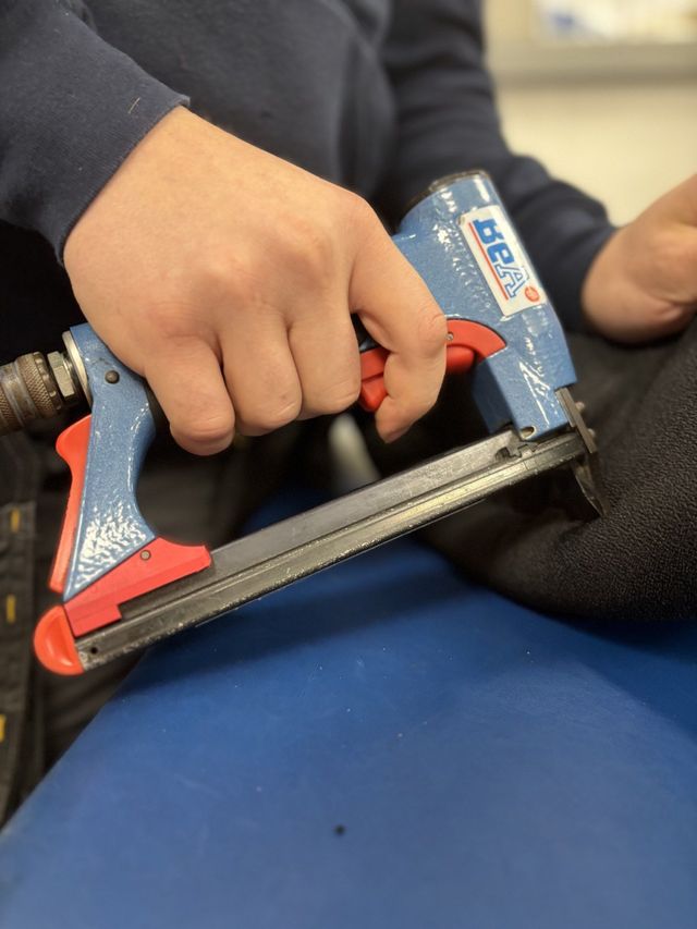 A seat pan being reupholstered with a staple gun